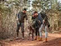Gothaer Jagdhaftpflichtversicherung: Drei Jäger mit ihren Jagdgewehren im Arm loben ihren Jagdhund